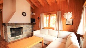 Un salón acogedor con chimenea de piedra, sofá blanco y vigas de madera.