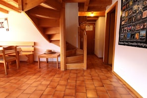 Una escalera de madera que conduce a un segundo piso, un banco de madera, una pequeña mesa con una cesta y una pared con cuadros enmarcados.
