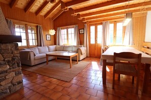 Un interior de madera acogedor, con una chimenea de piedra, un sofá, una mesa de centro y una mesa de comedor con sillas.