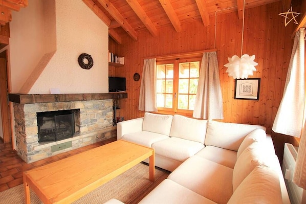 A cozy living room with a stone fireplace, a white sofa, and a wooden ceiling.