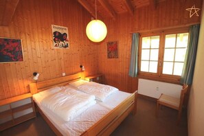 Una habitación de madera con una cama, un banco y un ventanal con cortinas.