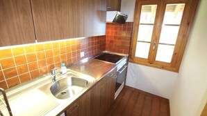 Una cocina compacta con armarios de madera, un lavamanos de acero inoxidable y un ventanal con persianas de madera.