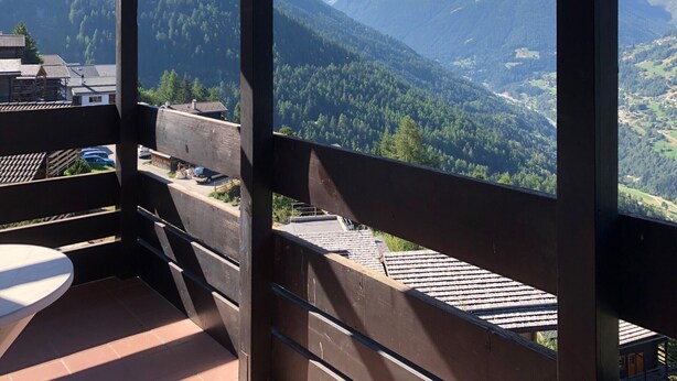 A balcony with a view of a mountainous landscape, wooden railings, and a tiled floor.