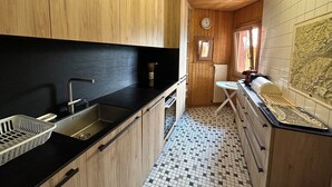 A compact kitchen with wooden cabinets, a black countertop, a tiled floor, and a small window.