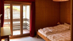 A wooden room with a bed, a desk, and a sliding glass door leading to an outdoor area.