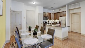 A modern kitchen with stainless steel appliances, a dining area with glass tables and chairs, and a small island with a sink. - Luxury 2BD w/ pool. 5 min walk to NRG Stadium. 10 min Dr to Downtown Houston!! (Houston)