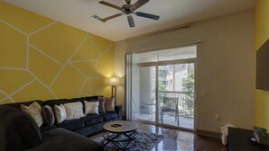 A living room with a dark sofa, a coffee table, and a ceiling fan. - Luxury 2BD w/ pool. 5 min walk to NRG Stadium. 10 min Dr to Downtown Houston!! (Houston)