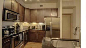 A modern kitchen with stainless steel appliances, wooden cabinets, and a granite countertop. - Luxury 2BD w/ pool. 5 min walk to NRG Stadium. 10 min Dr to Downtown Houston!! (Houston)