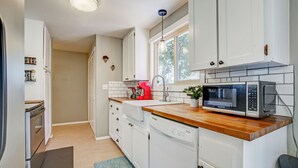 Uma cozinha moderna com armários brancos, bancada de madeira, micro-ondas embutido e cafeteira vermelha.