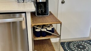 A kitchenette with a stainless steel refrigerator, a coffee maker on a small shelf, and a wicker cart holding jars.