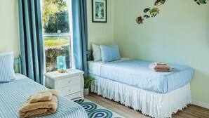 A bedroom with two beds, a window with curtains, a wall with fish decals, and a small table with a plant.