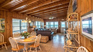 A wooden interior with a dining area, sofas, and a view of the ocean through large windows.