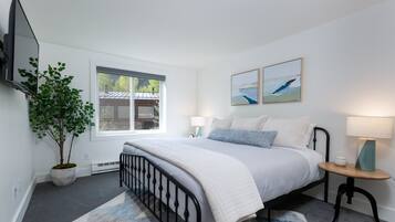 A bedroom with a bed, bedside tables, a TV, a window, and a potted plant.