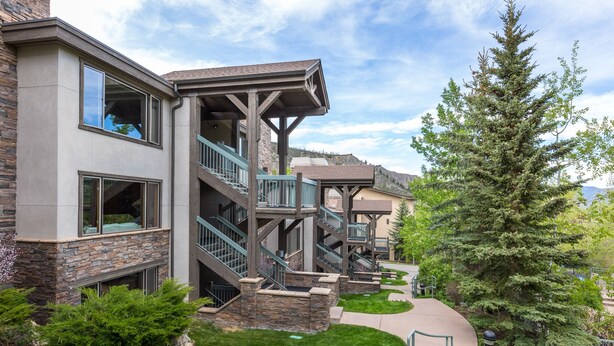A multi-story building with a stone facade, balconies, and a well-maintained lawn. - Stunning & Modern Family-Friendly Slopeside Retreat in the Heart of Snowmass! (Snowmass Village)