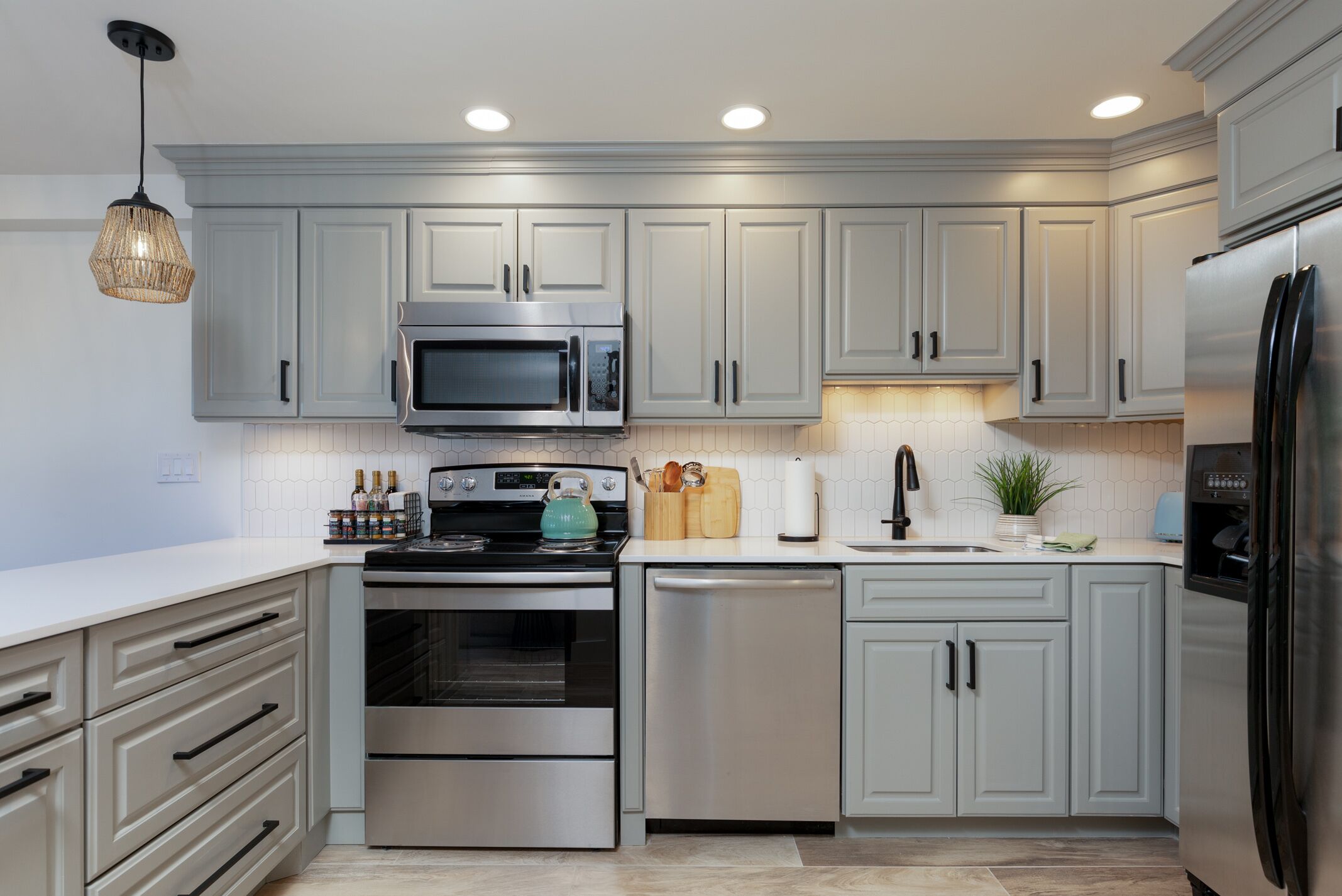 A modern kitchen with grey cabinets, stainless steel appliances, and a hanging light fixture.