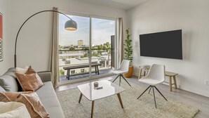 Een moderne woonkamer met een bank, twee fauteuils, een salontafel, een televisie en een groot raam met uitzicht op de stad.