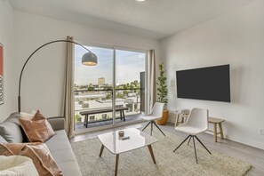 Un soggiorno moderno con un divano, due poltrone, un tavolino, una TV e un'ampia finestra con vista sulla città.