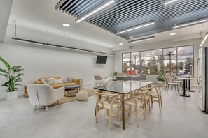 Uma sala de estar moderna com sofá, mesa de jantar e cadeiras, uma janela grande com vista e uma TV de tela plana na parede.