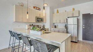 Een moderne keuken met een centraal eiland, barkrukken, roestvrijstalen apparatuur en hanglampen.