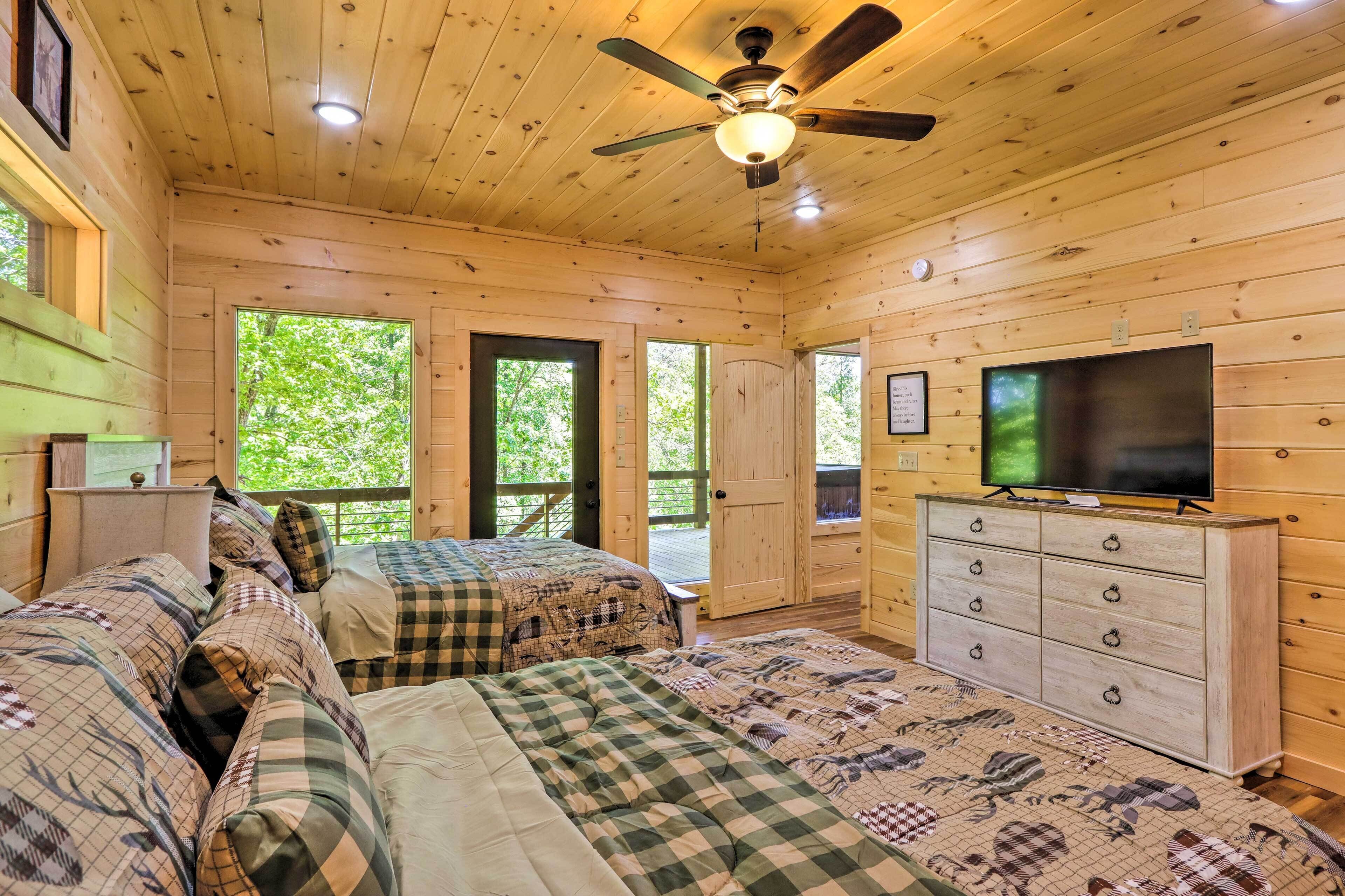 A cabin bedroom with two beds, a ceiling fan, a TV, and a dresser.