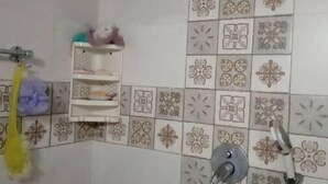 A bathroom with patterned tiles, a shower with a handheld showerhead, and a shelf with toiletries.
