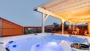 Un jacuzzi bajo un porche cubierto con sillas de madera y vistas a las montañas.