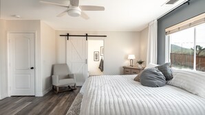 Un dormitorio con cama, una silla, una mesita de noche, una lámpara, un ventilador de techo y un ventanal.