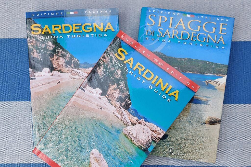 Three travel guides for Sardegna, Italy, titled 'Sardegna Guida Turistica', 'Sardinia Tourist Guide', and 'Spiaggia di Sardegna Guida Turistica'.