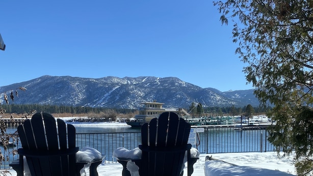 Deux fauteuils Adirondack sont placés face à un lac, avec un bateau amarré au loin et le sol recouvert de neige.