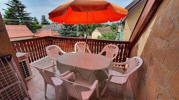 A balcony with a round table and six chairs, an orange umbrella, and a view of neighboring houses.