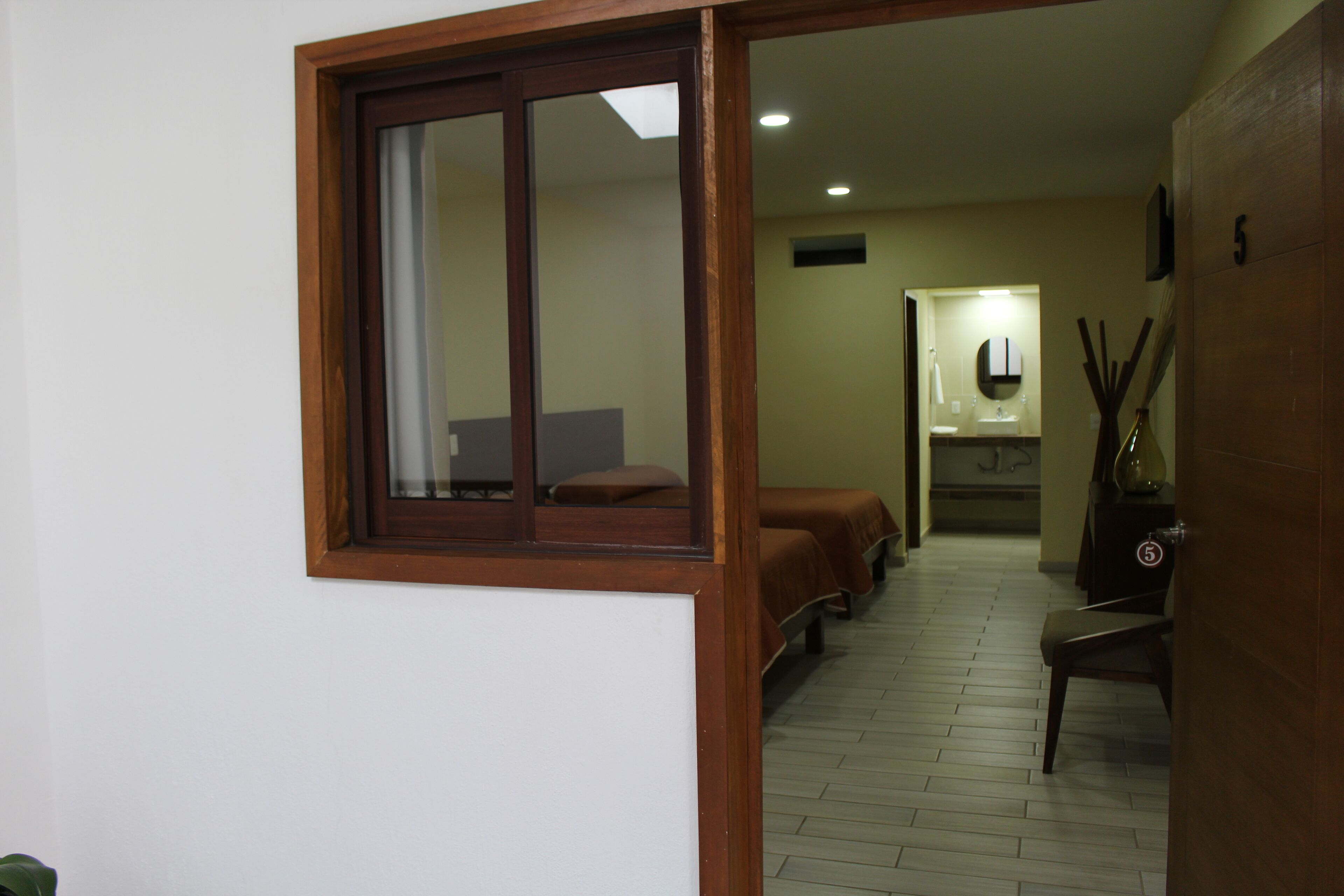 A hotel room with a wooden-framed window, a bed, a chair, and a small table.