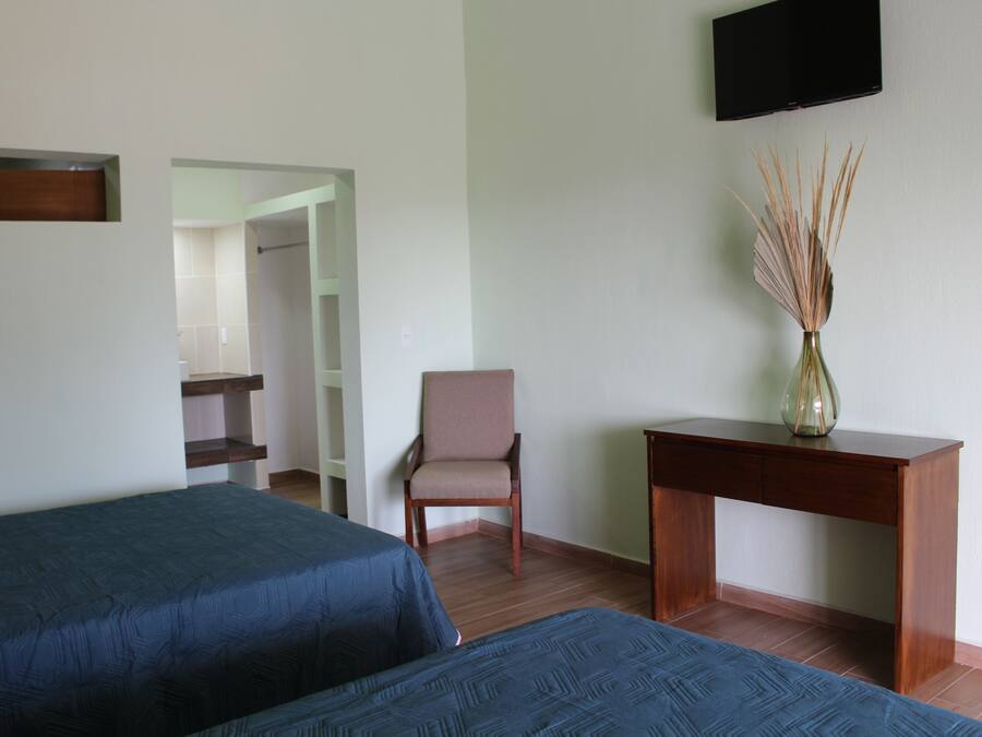 A room with two beds, a chair, a desk, and a television on the wall.