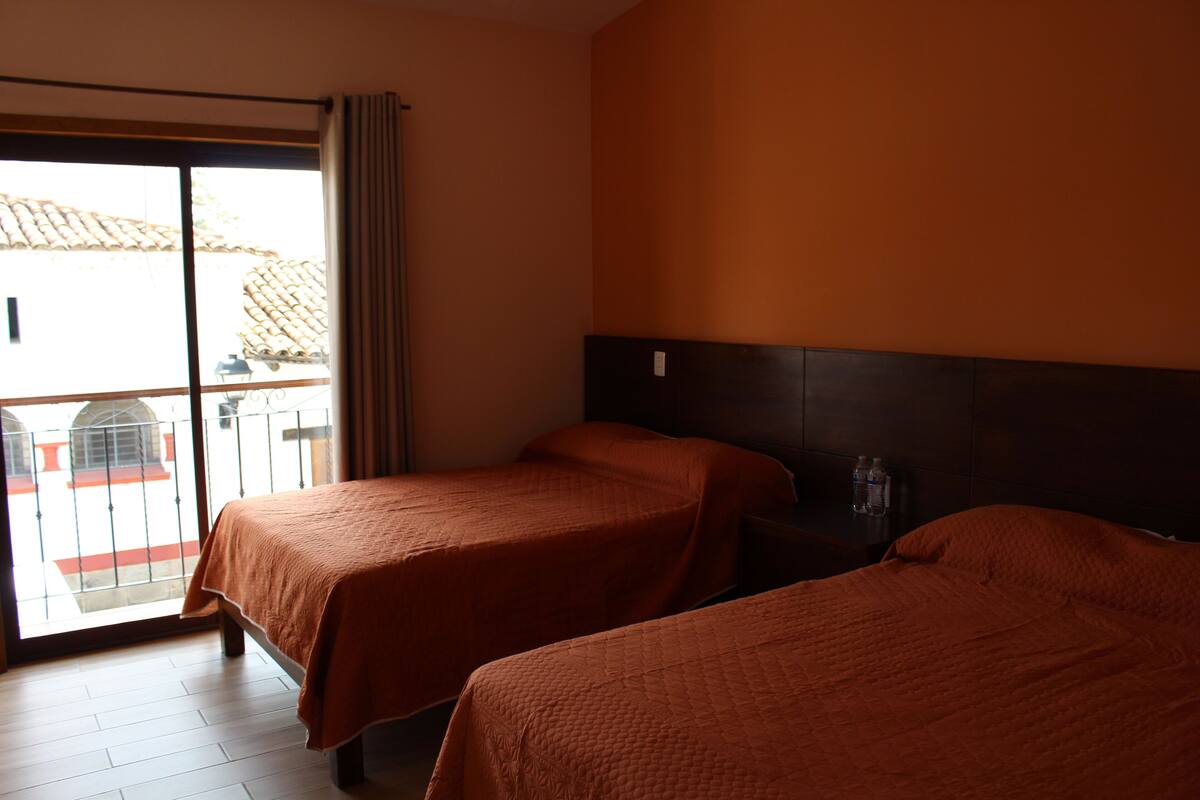 Una habitación de hotel con dos camas, un balcón con vistas y un ventanal grande.