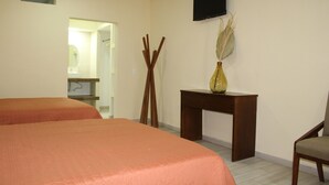 Una habitación de hotel con dos camas, un escritorio de madera, un televisor montado en la pared y un jarrón con plantas secas.