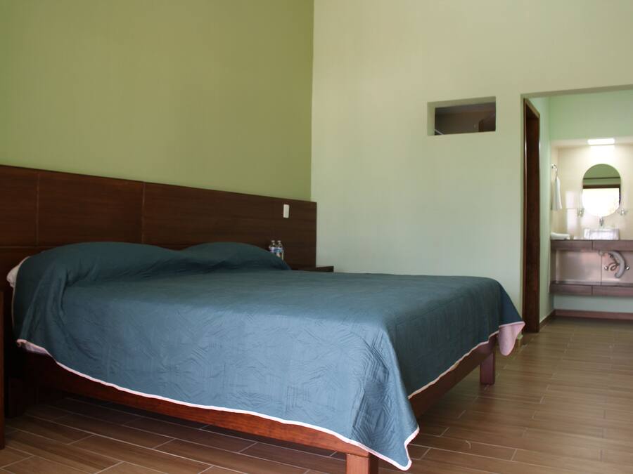 A bedroom with a wooden bed, a nightstand, a small bedside table, and a bathroom visible through an open door.