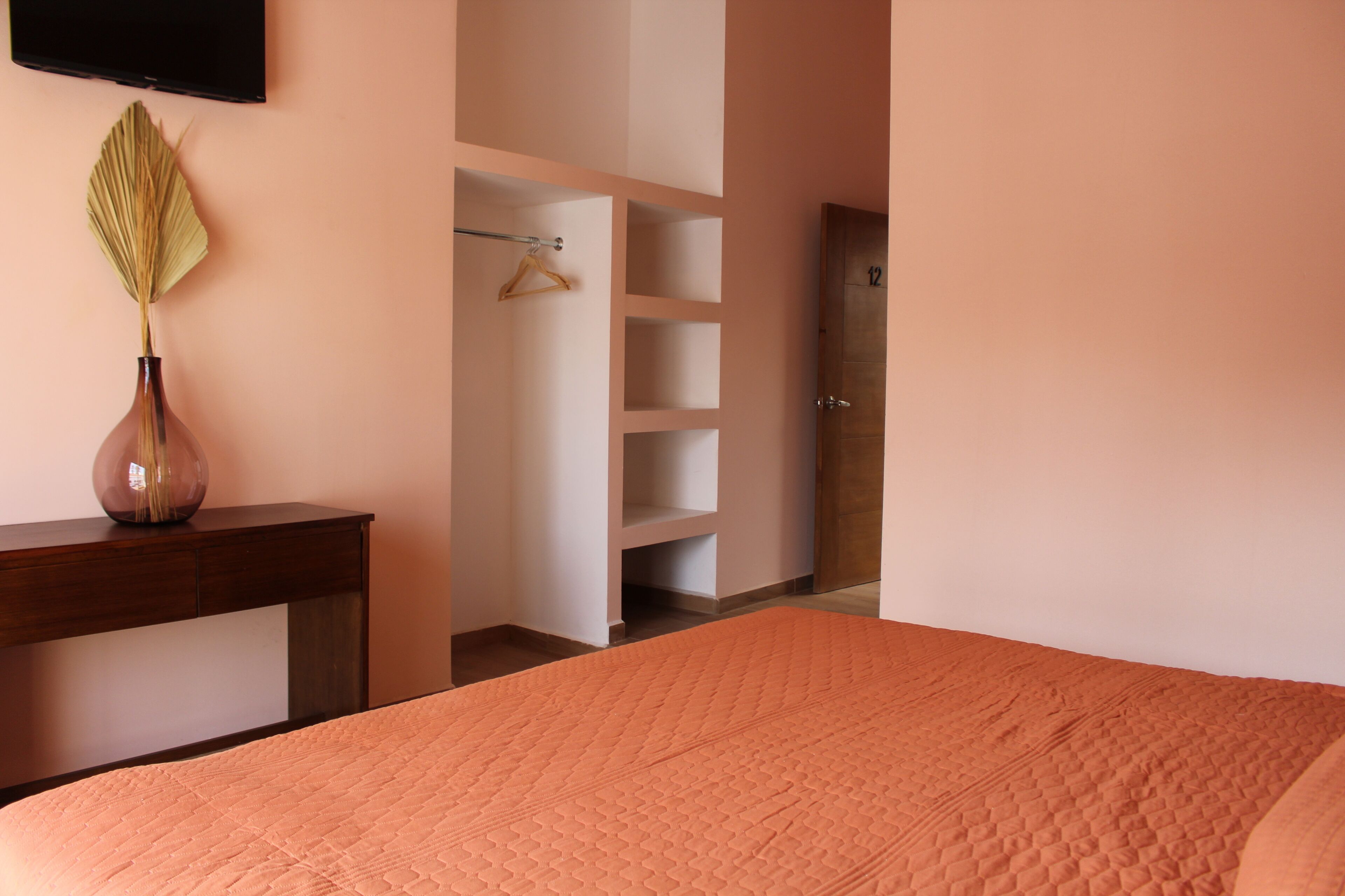 Un dormitorio con cama, cómoda, un florero con hojas secas y un armario con perchas.