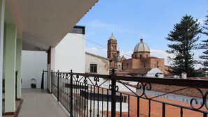 Un balcón con barandilla de metal que da a un patio con una iglesia y un árbol grande.