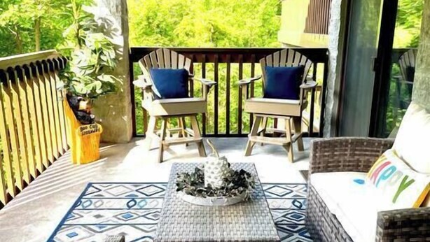 A covered outdoor seating area with wicker furniture, a central coffee table, and a view of greenery. - Heart of the mountain/5 Beds/Peaceful location with large deck (Gatlinburg)