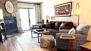 A cozy living room with a fireplace, leather sofas, patterned ottoman, and a 'Moose Trail' sign. - Heart of the mountain/5 Beds/Peaceful location with large deck (Gatlinburg)