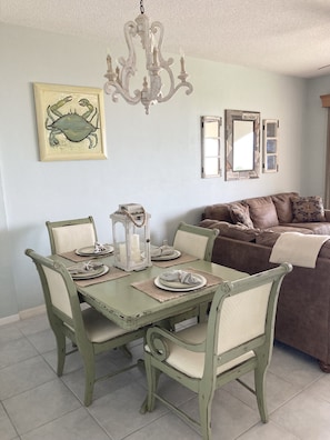 A dining area with a green table set for four, a chandelier, and a framed crab artwork on the wall.