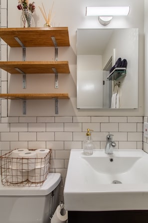 Un baño con un lavamanos blanco, un espejo y tres repisas de madera.