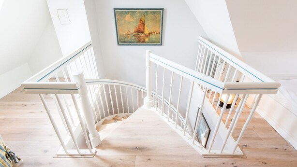 Eine weiße Treppe mit Glastrennwand, ein Segelboot-Gemälde an der Wand und ein Holzboden.