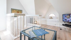 Ein modernes Schlafzimmer im Loft-Stil mit einem Glastisch, einem weißen Babybett, einem Bett mit rundem Fenster und einem Fernseher.