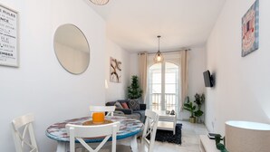 Ein modernes Wohnzimmer mit einem runden Tisch, weißen Stühlen, einem großen Spiegel und Blick ins Freie durch eine Glastür.
