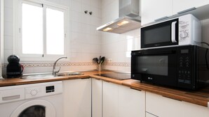 Eine kleine Küche mit weißen Schränken, einer Waschmaschine, einer Mikrowelle und einer Kaffeemaschine.