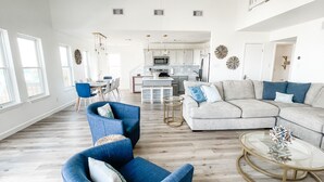 Amplia sala de estar con un sofá seccional gris, sillones azules y una mesa de centro de vidrio.