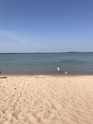 A sandy beach with a clear sky and calm sea. - The Bay Breeze. Walk to downtown Elk Rapids & Lake MI Beaches. Near Torch Lake, (Elk Rapids)
