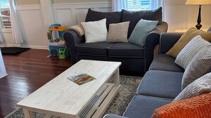 Ein Wohnzimmer mit einem dunkelgrauen Sofa, einem weißen Couchtisch und einem gemusterten Teppich.