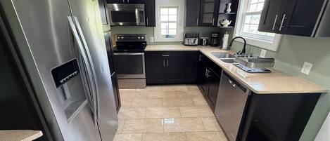 A modern kitchen with stainless steel appliances, dark cabinetry, and a tiled floor.