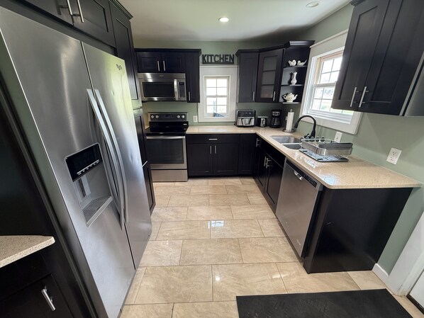 A modern kitchen with stainless steel appliances, dark cabinetry, and a tiled floor. - The Bay Breeze. Walk to downtown Elk Rapids & Lake MI Beaches. Near Torch Lake, (Elk Rapids)